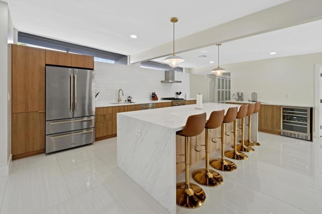 kitchen featuring appliances with stainless steel finishes, sink, a large island with sink, wine cooler, and hanging light fixtures