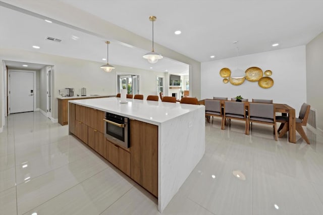 kitchen featuring light tile patterned flooring, hanging light fixtures, a large island, and stainless steel oven