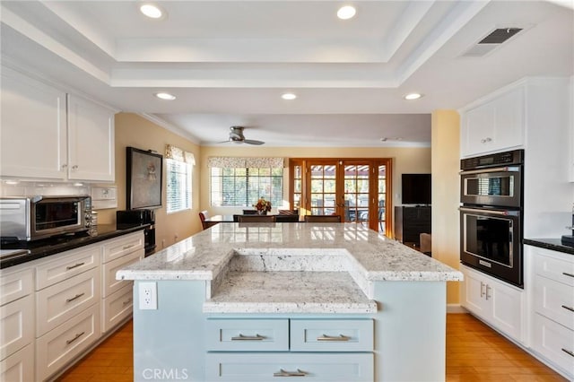 kitchen with ceiling fan, white cabinets, multiple ovens, and a kitchen island