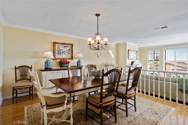 dining space featuring baseboards, visible vents, ornamental molding, wood finished floors, and a notable chandelier