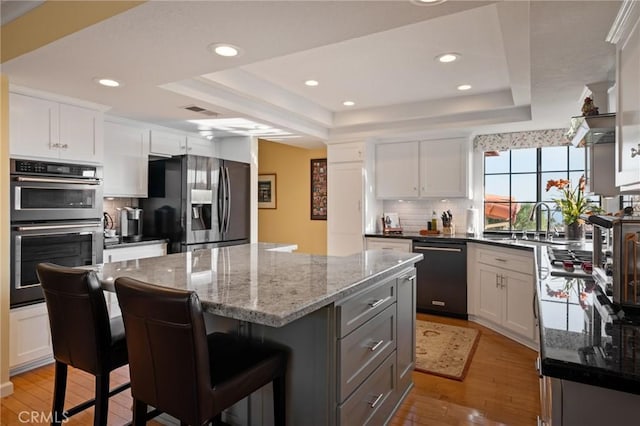 kitchen with black dishwasher, a raised ceiling, double oven, light wood-type flooring, and stainless steel fridge