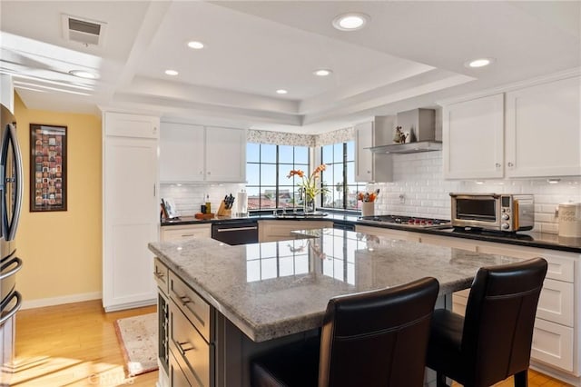 kitchen featuring wall chimney exhaust hood, visible vents, stainless steel gas stovetop, a kitchen island, and dishwashing machine