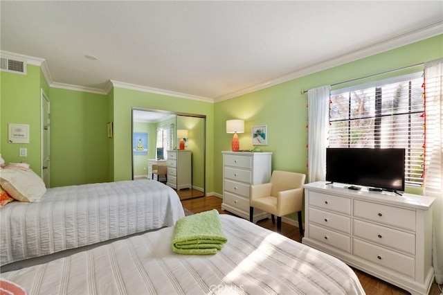 bedroom with a closet, visible vents, ornamental molding, wood finished floors, and baseboards