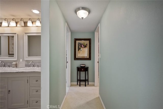 corridor with baseboards, a sink, and light colored carpet