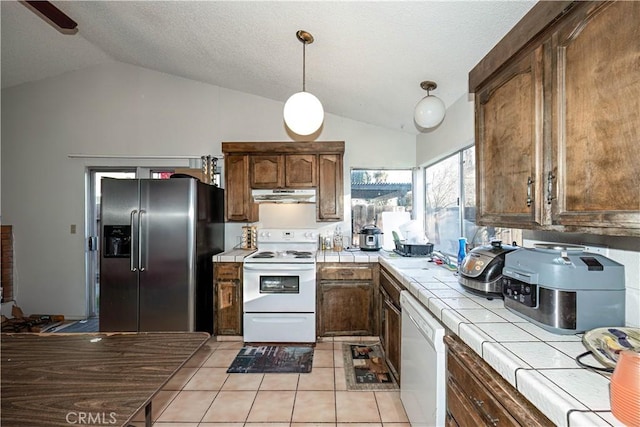 kitchen with tile countertops, lofted ceiling, white appliances, hanging light fixtures, and light tile patterned floors