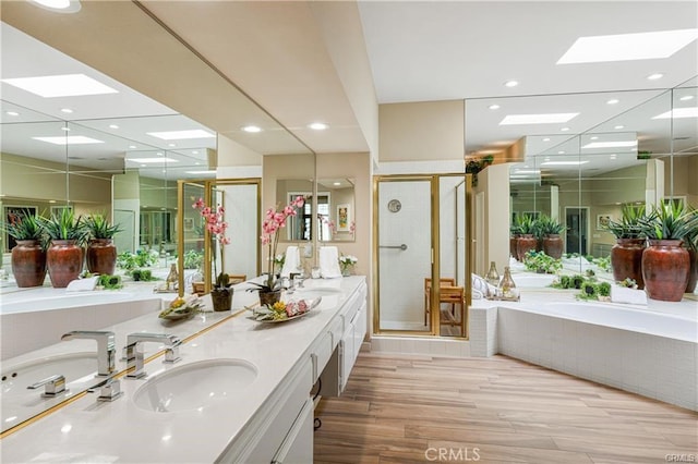 bathroom featuring double vanity, a stall shower, a sink, wood finished floors, and a bath