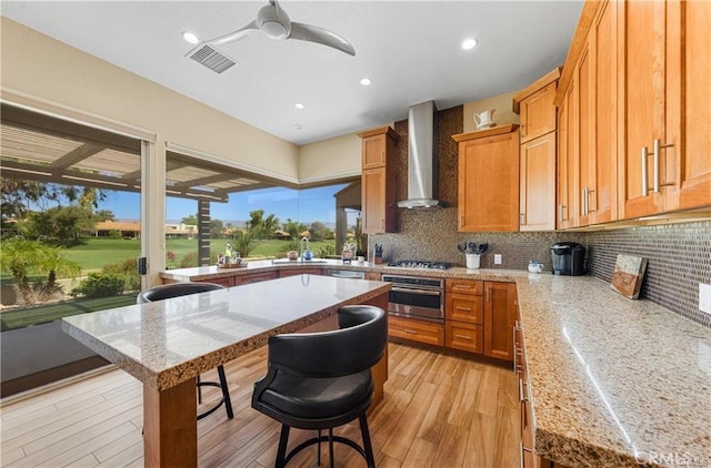 kitchen with visible vents, wall chimney exhaust hood, appliances with stainless steel finishes, a kitchen breakfast bar, and backsplash