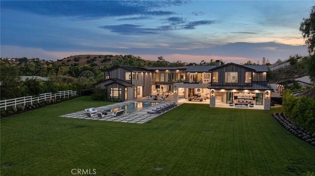 back house at dusk with a lawn, outdoor lounge area, a fenced in pool, a balcony, and a patio