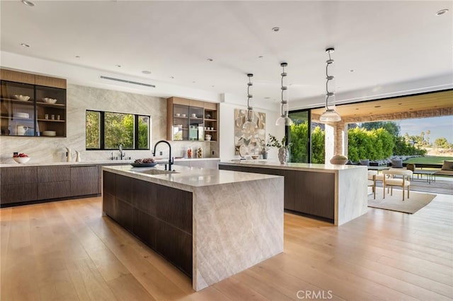 kitchen featuring decorative light fixtures, sink, a large island with sink, and light hardwood / wood-style flooring