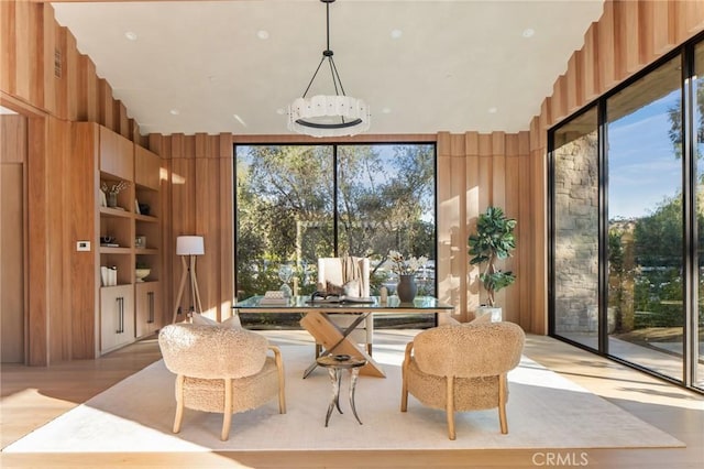 sitting room with built in shelves, light hardwood / wood-style flooring, expansive windows, a notable chandelier, and wood walls