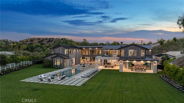 back house at dusk with an outdoor living space, a patio area, a fenced in pool, and a yard