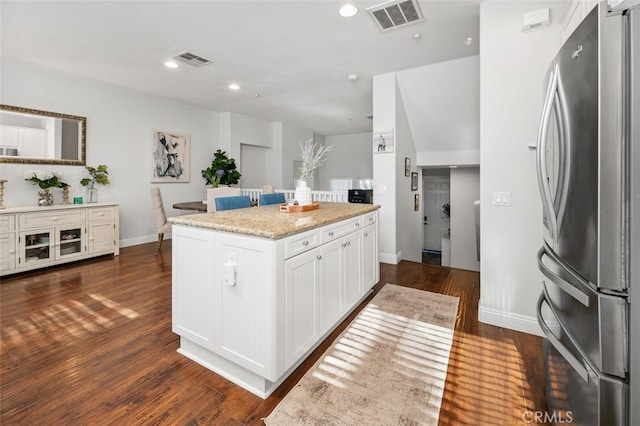 kitchen featuring a center island, light stone counters, dark hardwood / wood-style floors, stainless steel fridge, and white cabinets