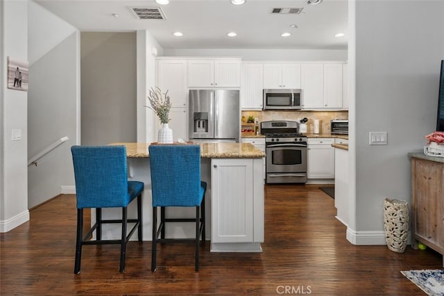 kitchen featuring a center island, stainless steel appliances, white cabinetry, and a breakfast bar area