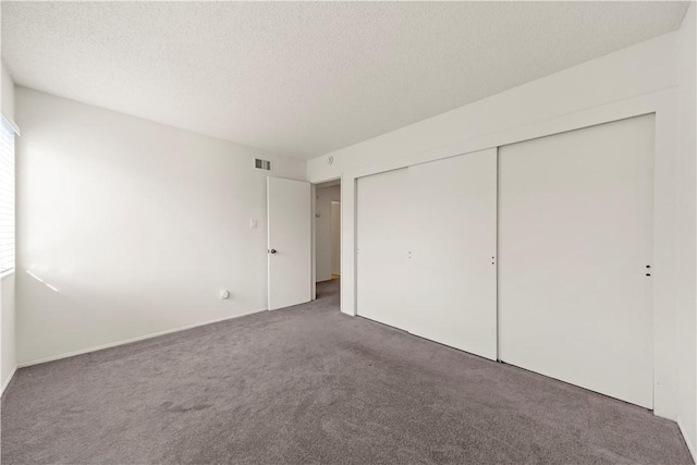 unfurnished bedroom featuring multiple windows, a closet, dark carpet, and a textured ceiling