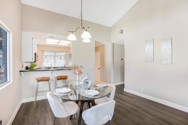 dining area featuring dark wood-type flooring, high vaulted ceiling, plenty of natural light, and an inviting chandelier