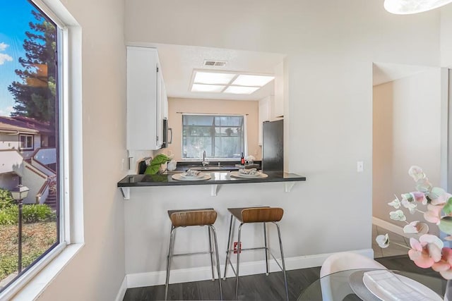 kitchen with refrigerator, white cabinetry, sink, kitchen peninsula, and dark wood-type flooring