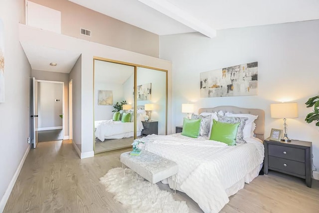 bedroom featuring light wood-type flooring, beam ceiling, and a closet