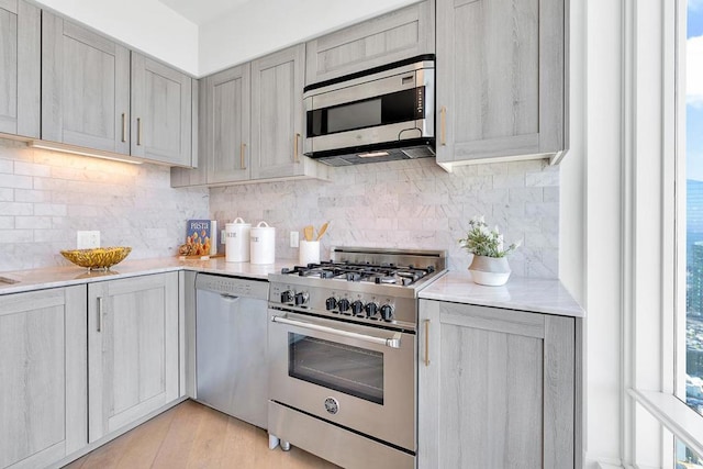 kitchen featuring light wood-type flooring, stainless steel appliances, gray cabinets, and tasteful backsplash