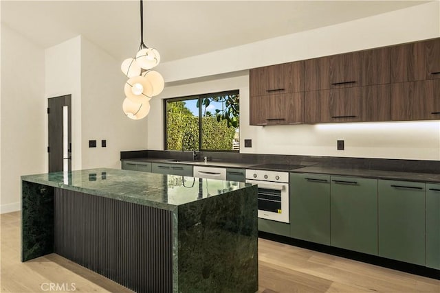 kitchen with pendant lighting, black stovetop, oven, a center island, and light wood-type flooring