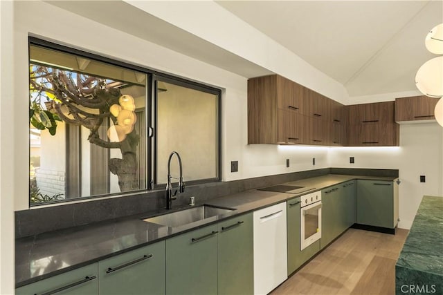 kitchen with sink, white dishwasher, wall oven, vaulted ceiling, and light wood-type flooring