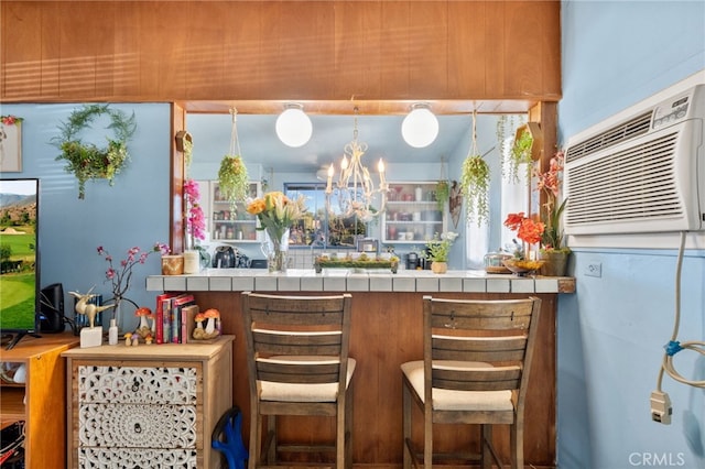 kitchen with tile countertops, a breakfast bar area, a wall mounted AC, and a chandelier