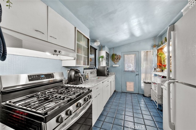 kitchen with gas range, sink, white cabinets, white fridge, and lofted ceiling