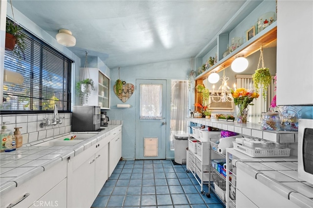 kitchen featuring sink, tile countertops, pendant lighting, lofted ceiling, and white cabinets