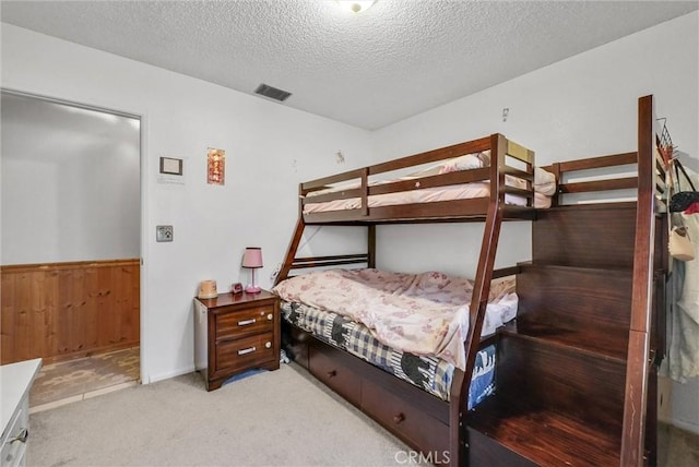 bedroom with light carpet, a textured ceiling, and wooden walls