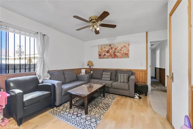 living room with a textured ceiling, light hardwood / wood-style floors, ceiling fan, and wooden walls