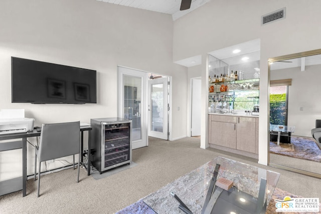 interior space with ceiling fan, beverage cooler, light colored carpet, and a high ceiling