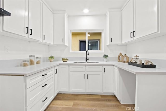 kitchen featuring white cabinets, wall chimney exhaust hood, light wood-type flooring, and sink