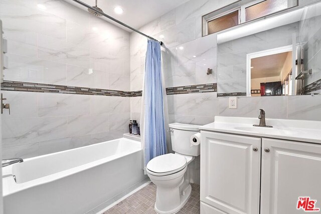 full bathroom featuring tile patterned flooring, shower / bath combination with curtain, toilet, vanity, and tile walls