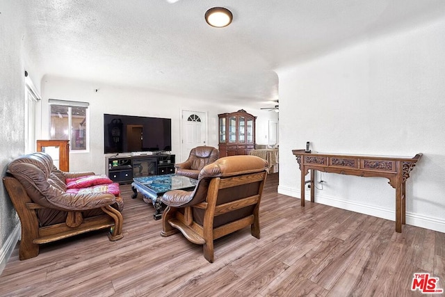 living room with a textured ceiling, light hardwood / wood-style floors, and ceiling fan