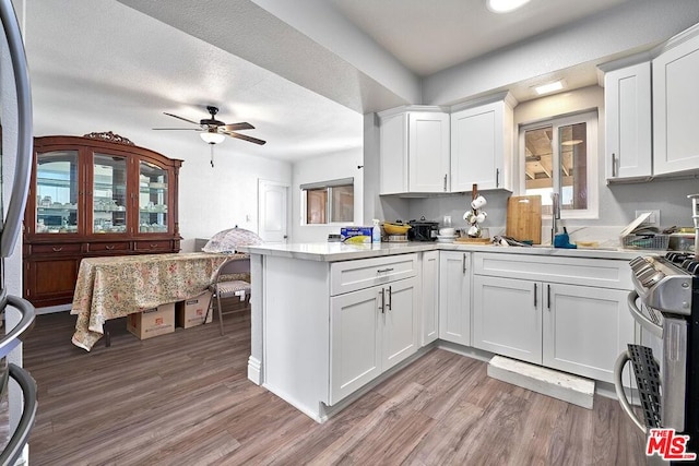 kitchen with white cabinets, light hardwood / wood-style flooring, ceiling fan, kitchen peninsula, and stainless steel appliances