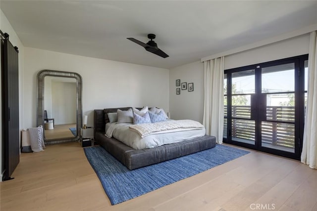 bedroom with access to exterior, light hardwood / wood-style floors, a barn door, and ceiling fan