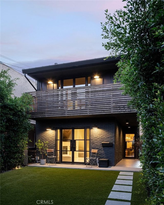 back house at dusk featuring a balcony, a yard, and a patio area