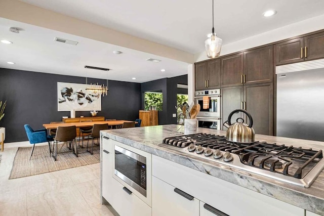 kitchen with built in appliances, white cabinets, dark brown cabinetry, and hanging light fixtures