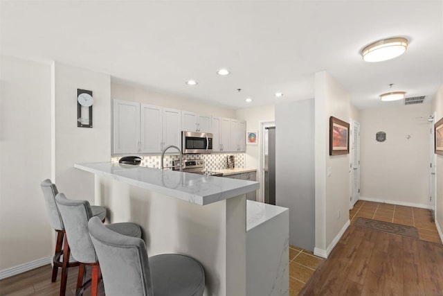 kitchen with a kitchen breakfast bar, kitchen peninsula, decorative backsplash, white cabinets, and appliances with stainless steel finishes