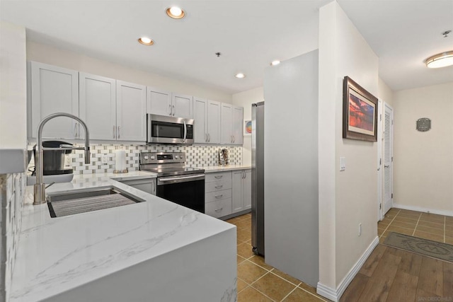 kitchen with sink, light tile patterned floors, tasteful backsplash, light stone counters, and stainless steel appliances