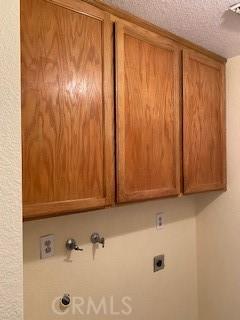 laundry room featuring hookup for an electric dryer, cabinets, a textured ceiling, and hookup for a washing machine