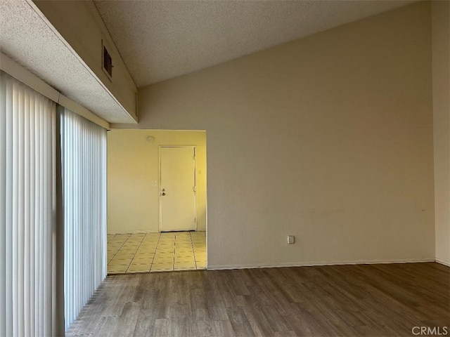 unfurnished room with a textured ceiling, light hardwood / wood-style floors, and lofted ceiling