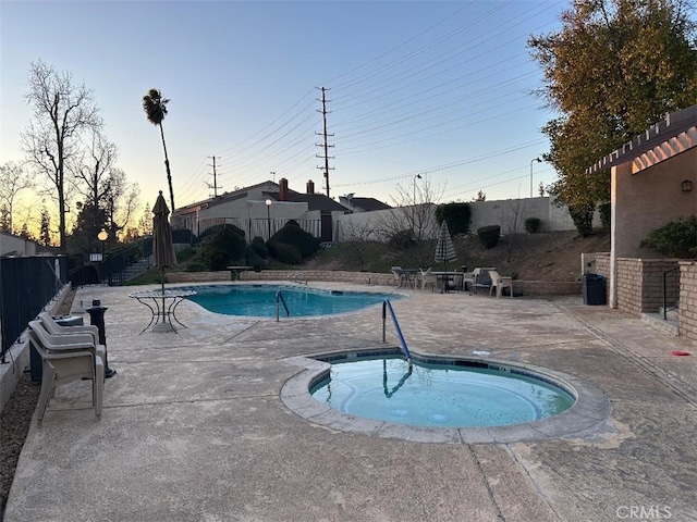 pool at dusk featuring a patio area and a hot tub