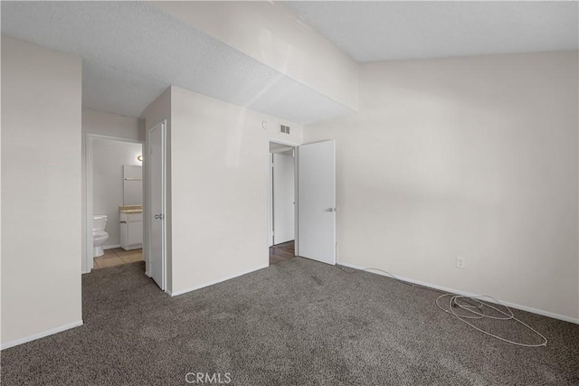 unfurnished bedroom featuring ensuite bathroom and dark colored carpet