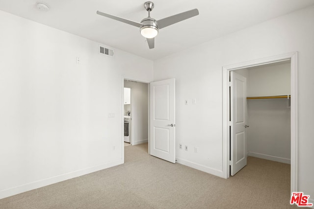 unfurnished bedroom with a walk in closet, light carpet, ceiling fan, and a closet