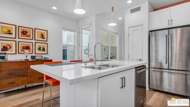 kitchen featuring sink, appliances with stainless steel finishes, light stone counters, an island with sink, and white cabinets