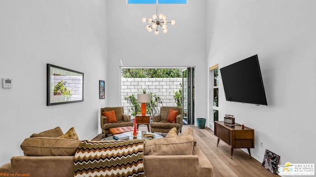 living room with an inviting chandelier, a towering ceiling, and light wood-type flooring