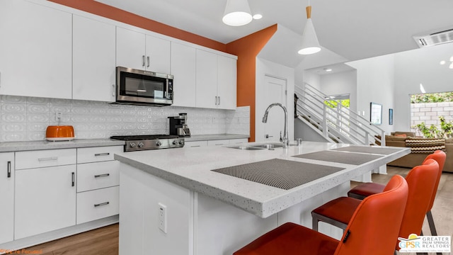 kitchen with white cabinetry, sink, a breakfast bar area, hanging light fixtures, and a center island with sink