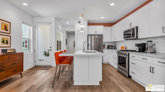 kitchen with a breakfast bar area, white cabinetry, stainless steel appliances, an island with sink, and decorative light fixtures