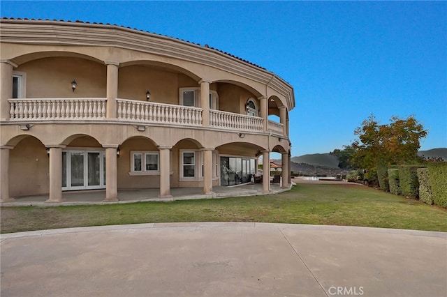 back of house featuring a mountain view, a yard, a balcony, and a patio