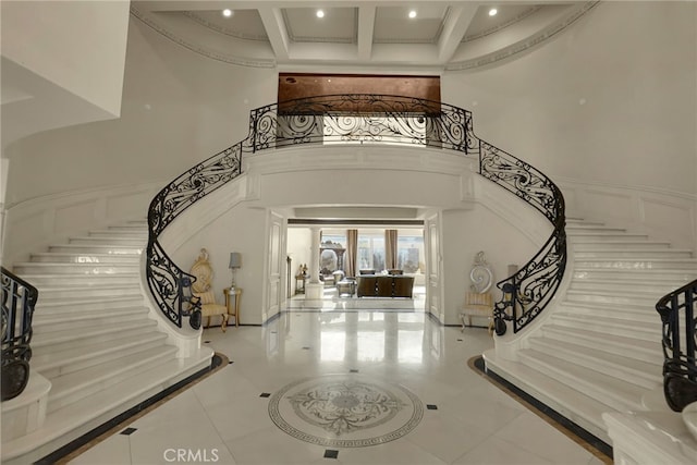 tiled entrance foyer featuring beamed ceiling, ornamental molding, a high ceiling, and coffered ceiling